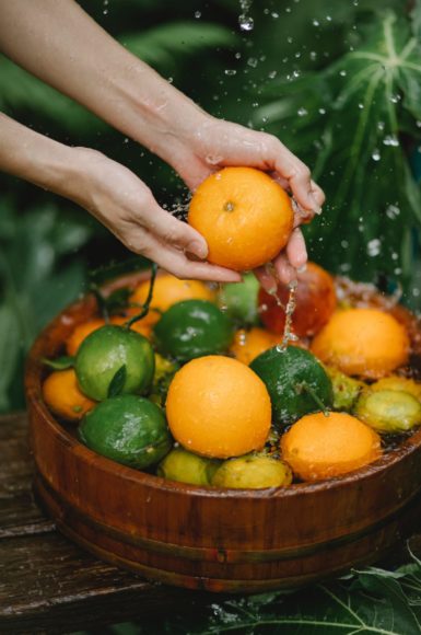 Mains lavant une orange au-dessus d’un panier d’agrumes