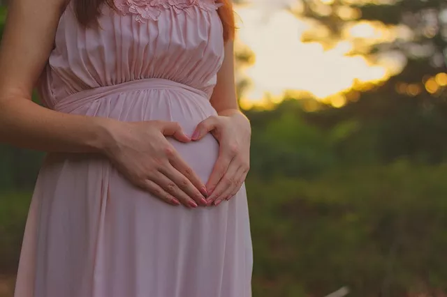 Femme enceinte en robe rose, mains sur le ventre