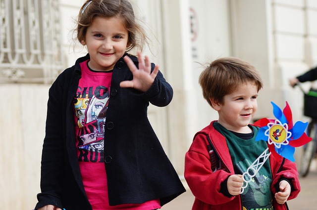 Deux enfants souriants, l’un agitant la main, l’autre un moulin