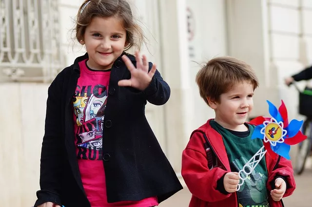 Deux enfants souriants, l’un agitant la main, l’autre un moulin