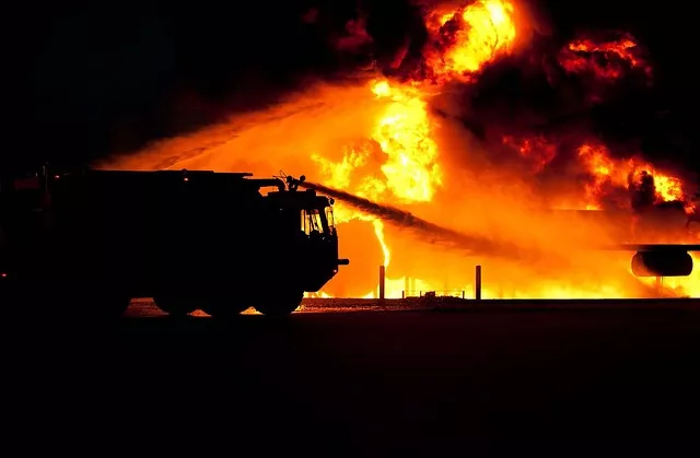 Camion de pompiers devant un immense incendie nocturne